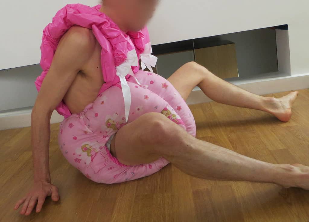 Graney is lying down on the floor, wearing an adult big diaper in pink.