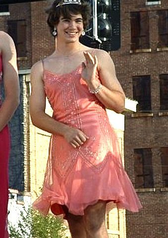 On the ground beside the roadside, a man who has been gendered is standing like a woman.