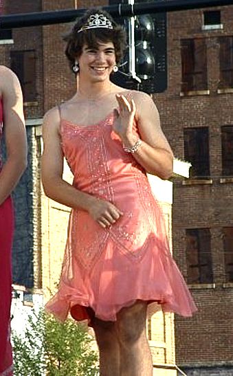 On the ground beside the roadside, a man who has been gendered is standing like a woman.