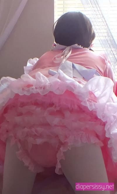 Standing on the ground in a frill baby gown and donning a white stocking and diaper