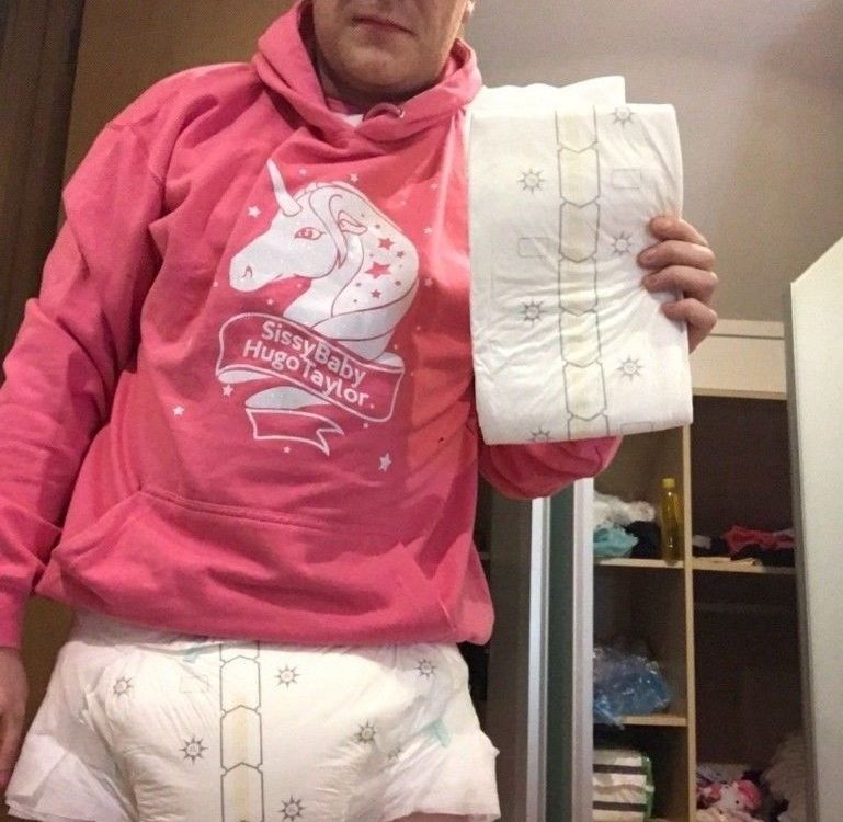 A man who loves diapers is standing on the ground while donning a pink dress and a diaper.